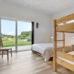 Zimmer mit Doppelbett und Schlafcouch, großes Fenster mit Blick auf Grünflächen.