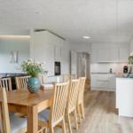 Essbereich mit Holztisch und Stühlen. Küche mit weißen Schränken. Wohnbereich mit Sofa und Fenster.