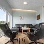 Wohnzimmer mit Sofa, zwei Sesseln und großem Fenster zur Außenterrasse.