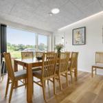 Esszimmer mit Holztisch, Stühlen und großem Fenster. Wandregale und Bilder an den Wänden.