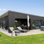 Moderne Villa mit Terrasse, Liegen, Grill und Whirlpool. Grünfläche und klarer Himmel.
