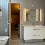 Bad mit Waschbecken, Spiegel und Toilette. Durchgang zur Sauna.