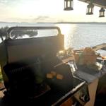 Grill mit Mais und Fisch auf Terrasse mit Blick auf See.