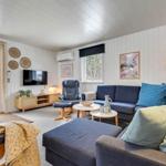 Wohnzimmer mit Sofa, Sessel und TV. Fenster und Tür zu Außenbereich.