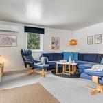 Wohnzimmer mit blauem Sofa, zwei Sesseln und Holztisch. Wandbilder und Pflanzen.