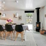 Esszimmer mit Esstisch, Stühlen und Kaminofen. Große Fenster und helle Wände.