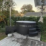 Schwarzer Whirlpool auf Holzterrasse mit Pflanzen und Holzdekor