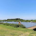 Holzsteg führt zu einem See mit Booten und Grünflächen.