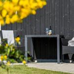 Außenbereich mit Tisch und zwei Stühlen vor schwarzem Holzhaus. Gelbe Blumen im Vordergrund.