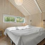 Bedroom with wooden walls and sloped ceiling. Bed, nightstand, stool, and wardrobe.