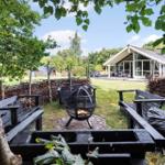 Behind a wooden fence is a fire pit with burning wood. In the background, a house with a terrace is visible.