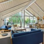 Living and dining area with blue sofas, wooden walls, and large windows.