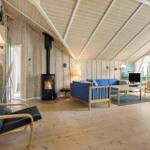 Living room with wood walls, fireplace, and blue sofa. Wooden floor and large windows.
