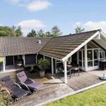 Modern villa with large wooden deck, garden furniture, and view of trees.