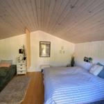 Schlafzimmer mit Dachschrägen, Bett und kleinem Sofa. Holzfußboden und weiße Wände.
