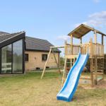 Haus mit Spielplatz, blauer Rutsche und Schaukel im Garten.