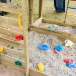 Holzspielplatz mit Sandkasten und bunten Kinderspielzeugen