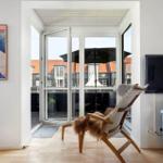 Wohnzimmer mit Sessel, Fernseher und Blick auf Balkon mit Sonnenschirm.