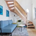 Ein Wohnzimmer mit blauem Sofa, Holztreppe und Wandbildern.