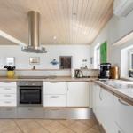 Küche mit weißen Schränken, Holzoberflächen und Edelstahlgeräten unter Holzdecke.