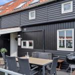 Außenbereich mit Tisch, Stühlen und Grill vor einem Haus mit dunkler Fassade und rotem Dach.