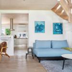 Wohnzimmer mit Sofa, Tisch und Stuhl. Küche und Essbereich sind sichtbar. Holzdecke und Treppenhaus.