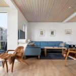 Ein Wohnzimmer mit blauem Sofa, zwei Holzstühlen mit Fell, Holzboden und großen Fenstern.