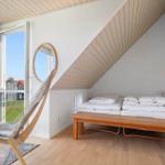 Schlafzimmer mit Dachschräge, Bett, Holzbank und großem Fenster mit Blick auf Garten.