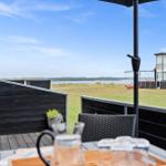 Terrasse mit Tisch und Stühlen, Blick auf Grünfläche und Wasser.