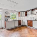 Küche mit weißen Schränken, Holzfronten, Arbeitsplatte und Fenstern.