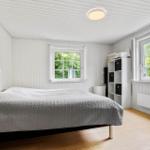 Schlafzimmer mit Bett, Fenstern und Holzboden.