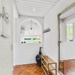 Eingangsbereich mit Spiegel, Holzständer und Terrakottafußboden. Fenster und Decke sind weiß.