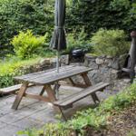 Holztisch mit Bänken, Grill und Feuerkorb im Garten.