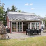 Haus mit Terrasse, Grill und Garten. Große Fensterfront zur Außenseite.