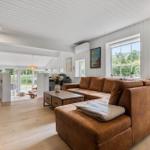 Wohnzimmer mit braunem Sofa, Holzboden und weißen Wänden. Fenster mit Blick auf Garten.