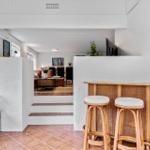 Barbereich mit Hocker und Getränkehalter, Blick in Wohnzimmer mit Sofa und Treppe.