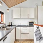 Küche mit weißen Schränken, Edelstahlspüle und Mikrowelle. Holzfenster und Decke.