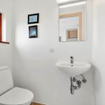 Badezimmer mit Toilette, Waschbecken und Spiegel. Fenster mit Holzrahmen.
