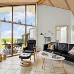 Wohnraum mit schwarzer Ledercouch und Sessel, großes Fenster mit Blick auf Terrasse und Landschaft.