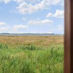 Blick aus dem Fenster auf Feld und See mit Windrädern im Hintergrund.