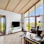 Wohnzimmer mit großem Fensterblick auf Grasland und Terrasse mit Sitzmöbeln.