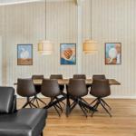Dining room with wooden wall, table, six chairs, three wall pictures, and two pendant lights.