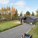 Modern villa with wooden veranda and garden. Green lawn and trees surround the house.
