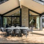 Deck with table and chairs under roof, glass walls and wooden floor.