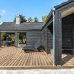 Modern villa with wooden terrace, lounge chairs, and garden furniture. Black facade and large outdoor area.