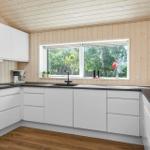 Kitchen with white cabinets, dark countertop, and wood paneling. Window with view of trees.