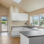 Modern kitchen with white cabinets and dark worktop. Wooden walls and large windows.