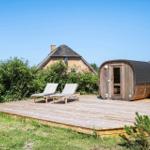 Holzterrasse mit Liegestühlen und Sauna neben einem Haus mit Schindeldach.