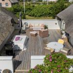 Terrasse mit Sitzgruppe, Tisch, Grill und Blick auf Grünflächen.