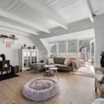 Wohnzimmer mit Kamin, Sofa und Rattanmöbeln. Holzboden und weiße Wände.